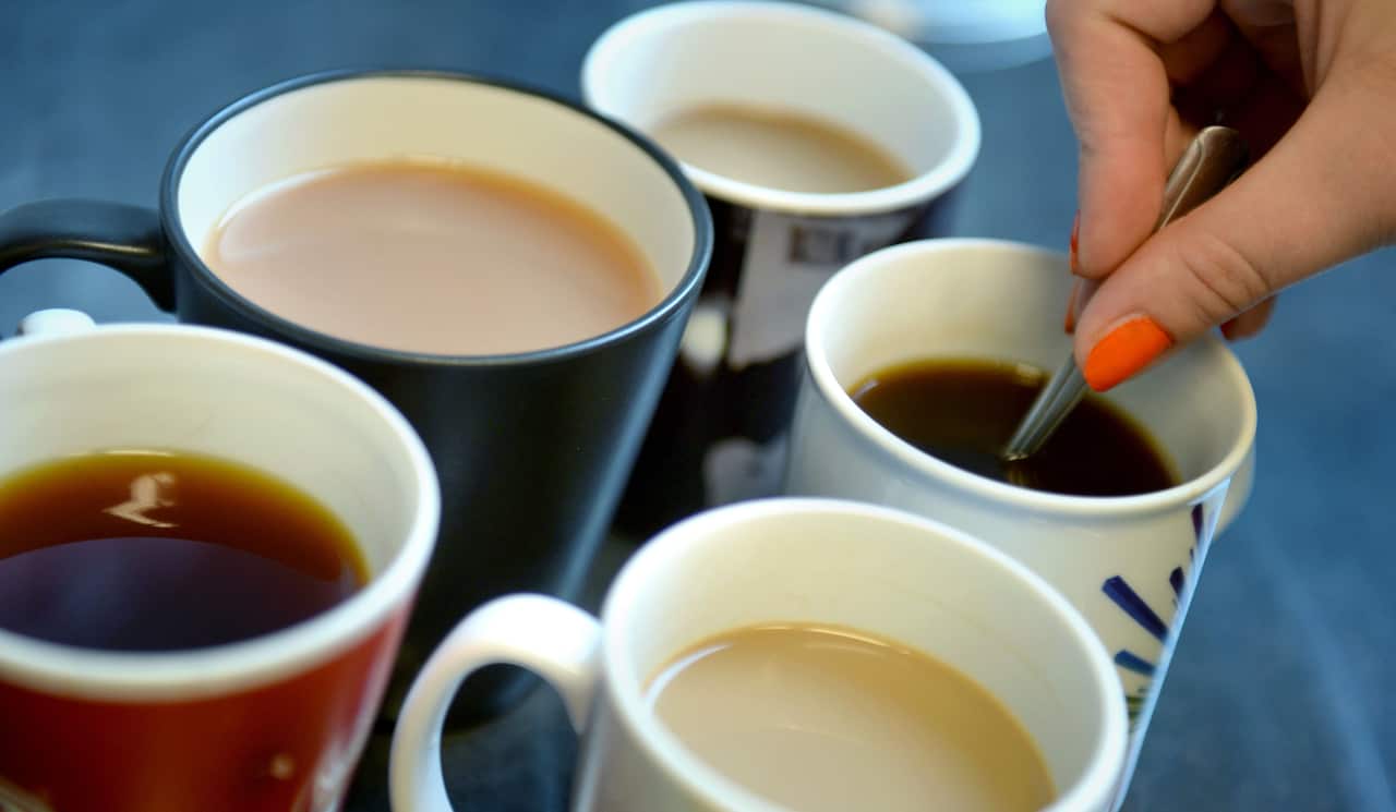A woman stirs cups of tea and coffee