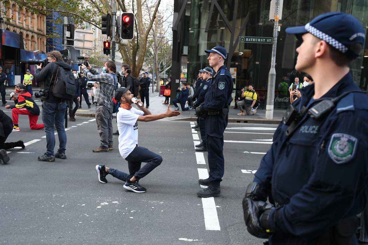 Man kneels and offers hand to officer in Sydney at the Black Lives Matter protest. 
