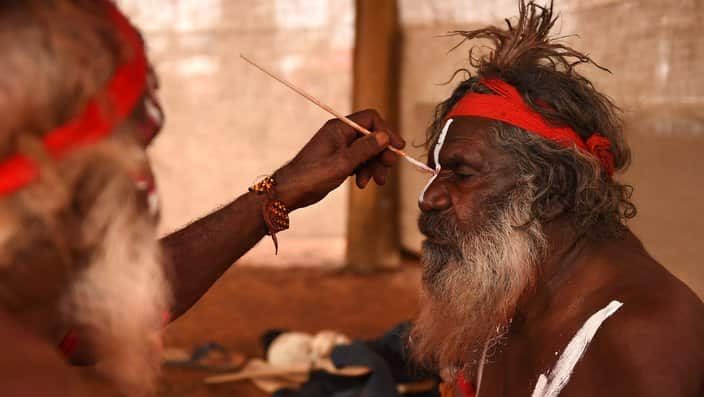 An Aboriginal elder paints a fellow elder before dancing at a cultural event near Uluru