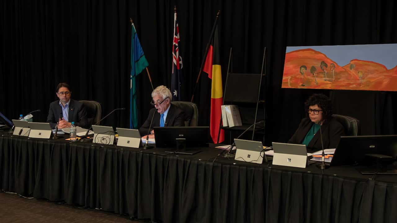 Three people are seated behind a long table
