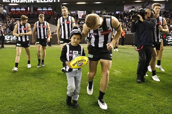 Collingwood mascot, Kyron McGuire, runs out on to the field with Adam Treloar of the Magpies. 