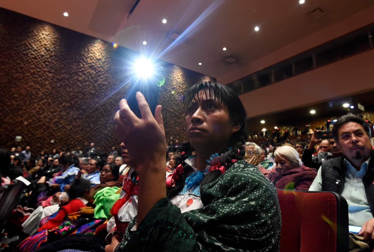 Relatives of Hnahnu indigenous woman Jacinta Francisco, Alberta Alcantara and Teresa Gonzalez take pictures with their phones.
