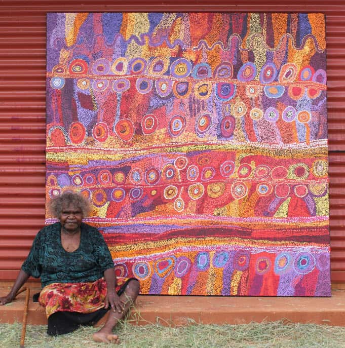 Wawiriya Burton sitting in front of 'Ngayuku Mamaki Ngura - My Father's Country' (2012).