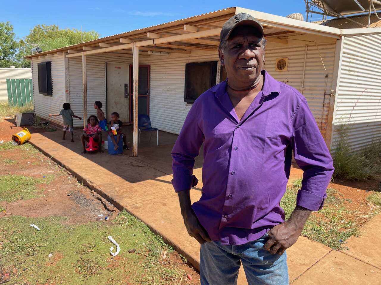 A man stands in front of a house with children in the background