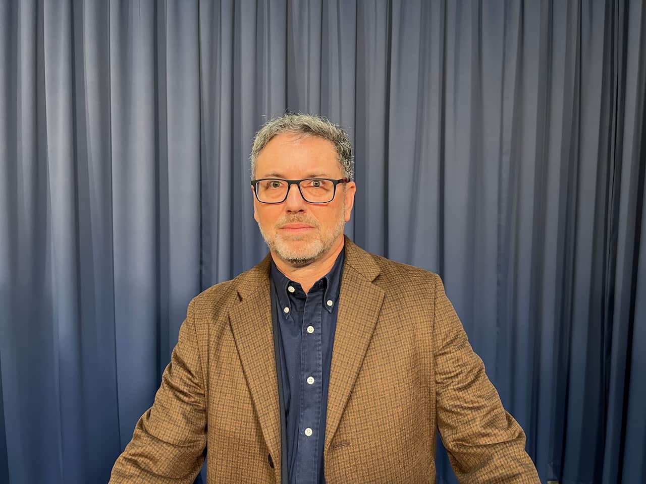 A man is wearing glasses, a suit jacket and buttoned up shirt