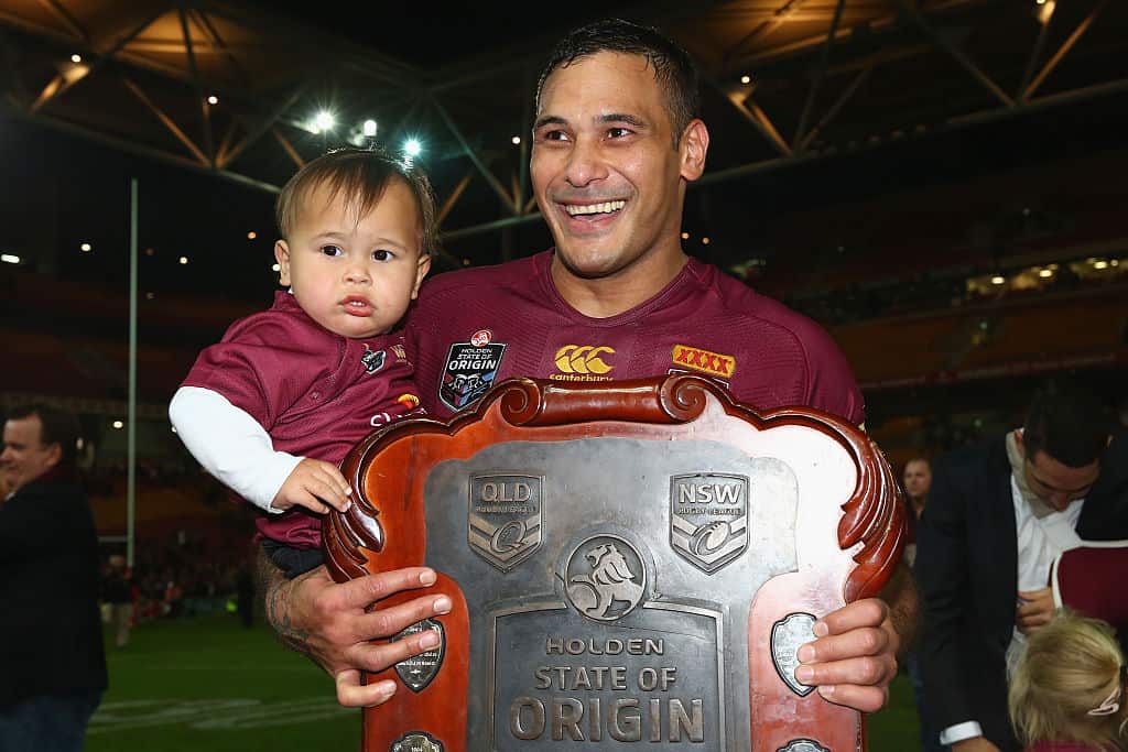 Justin hodges holds the state of origin shield and his son on the football pitch