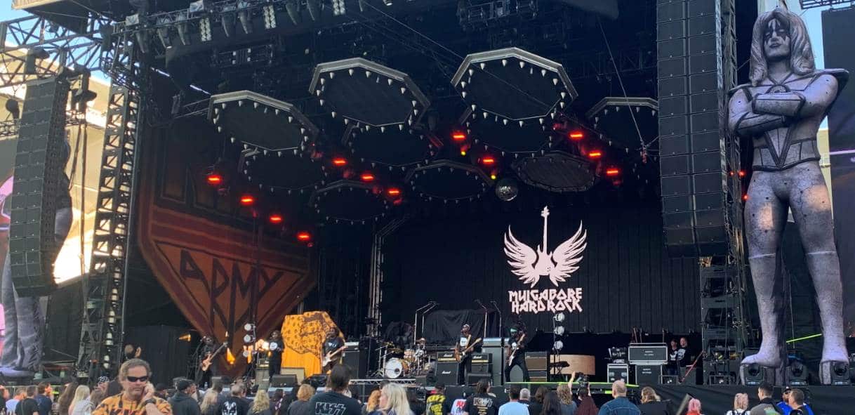 A long shot of Mulga bore band playing on stage before a crowd, with their band's name done in the typical KISS font on a sign 