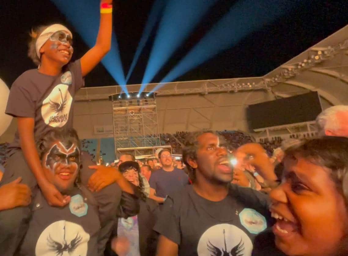The mulga bore band in kiss makeup sing and dance in the crowd while watching their idols perform. 