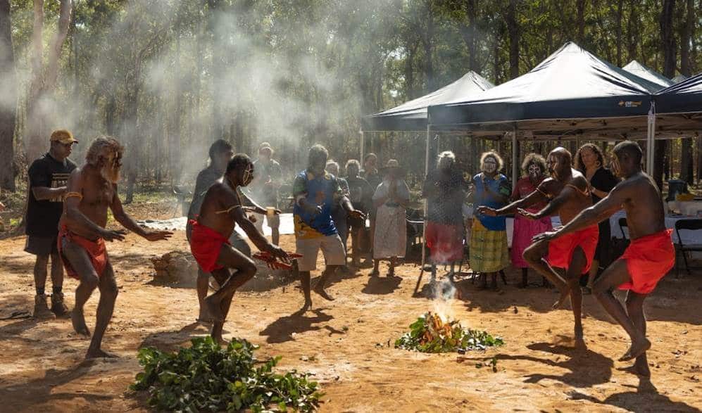 Traditionally face-painted men and women dancing around a smoking bush of leaves, with temporary gazebos erected nearby