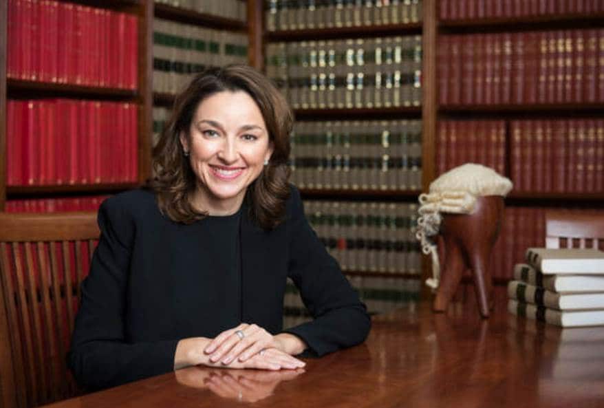 peggy dwyer sitting at a desk with a barrister's wig and shelves full of legal volumes behind her. 