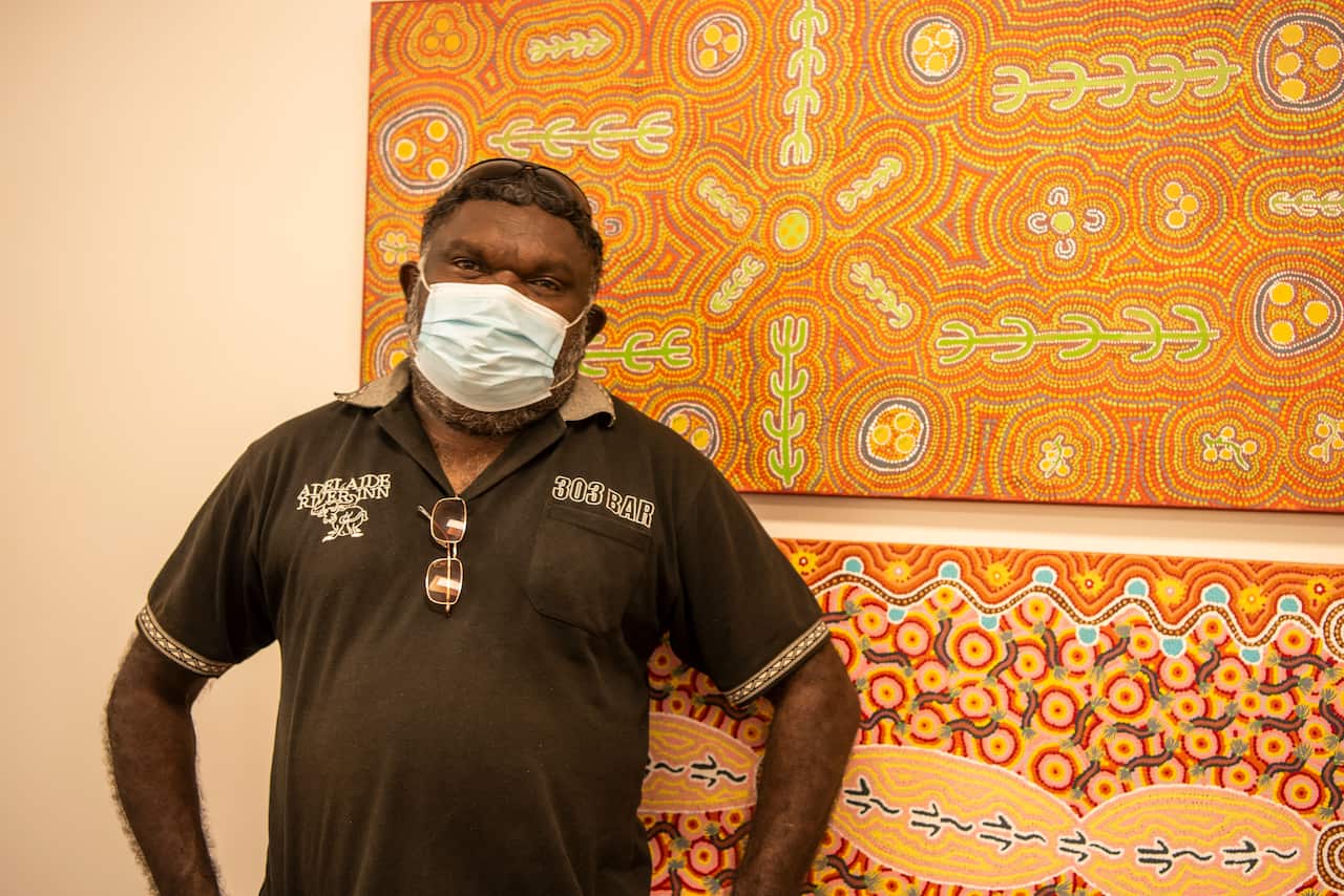 Rob Roy stands in front of artworks wearing a facemask. 