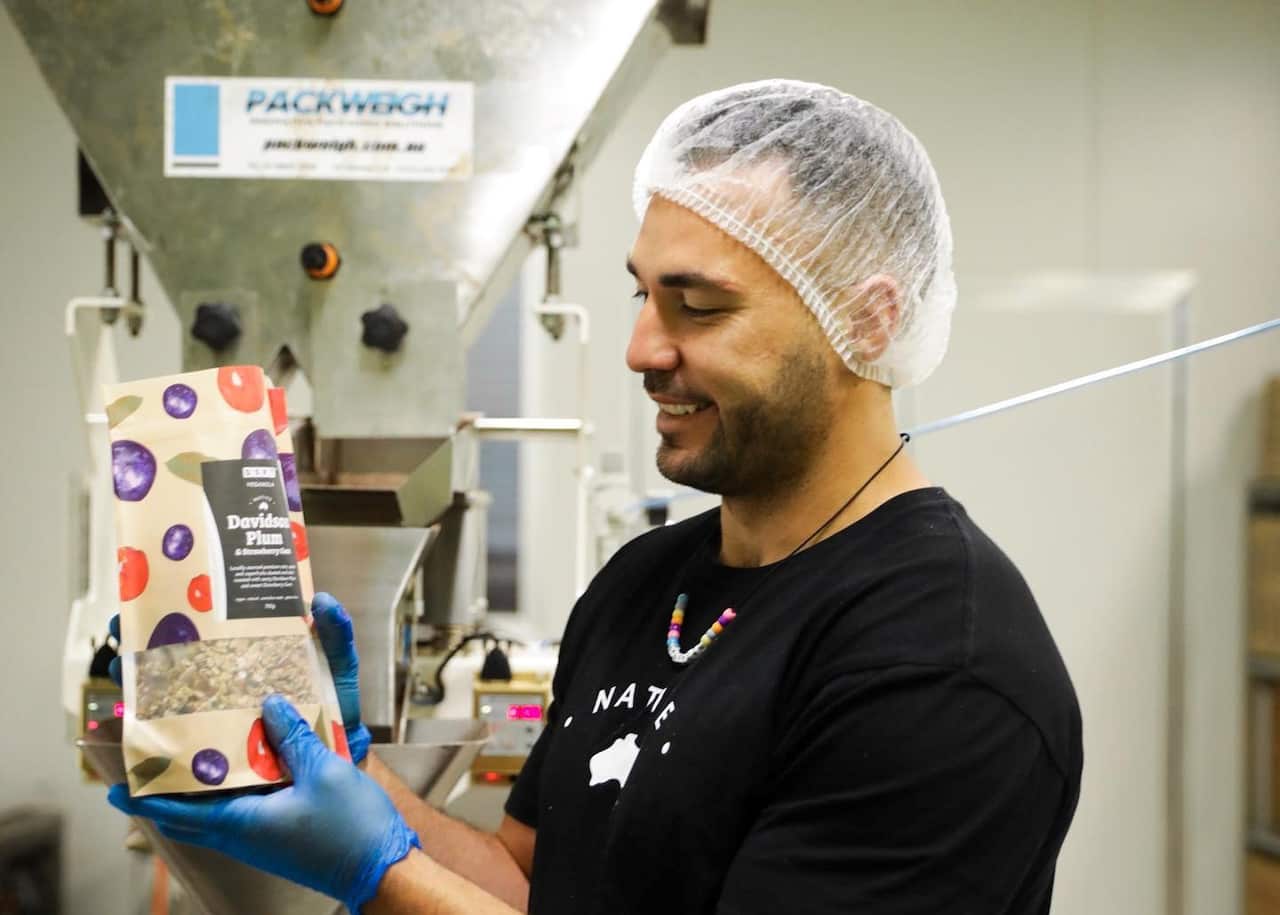 Ryan James wearing a hair net and gloves holds up a packet of granola
