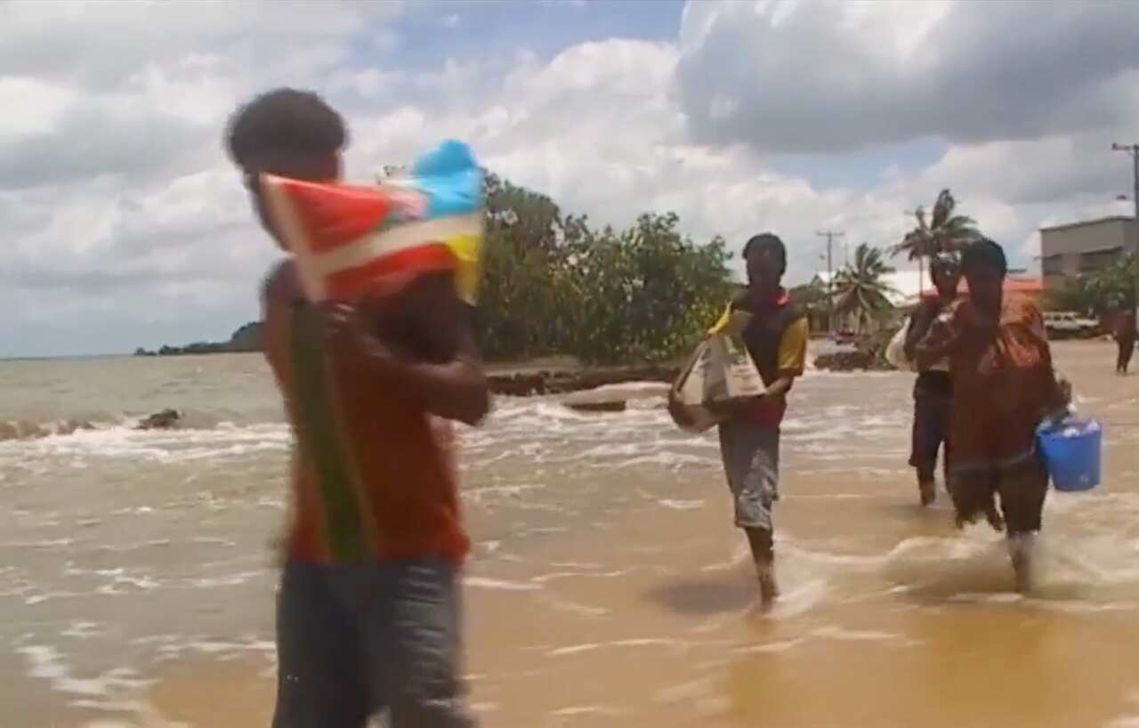 Torres strait Islanders carry supplies as a high tide washing over a sea-wall and into the community. 