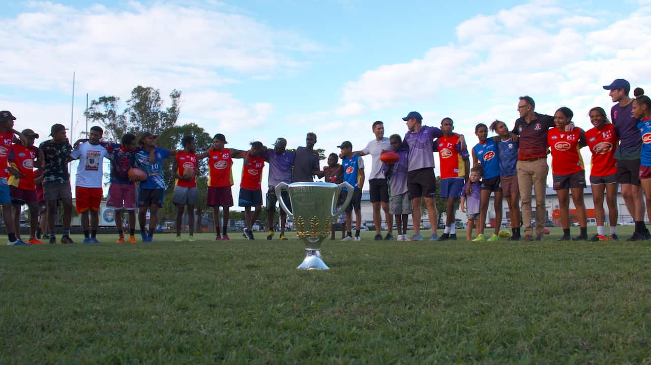 AFL Cape York House boys and girls surround the 2020 Premiership Cup with ex-premiership player and Brownlow Medallist, Simon Black. 