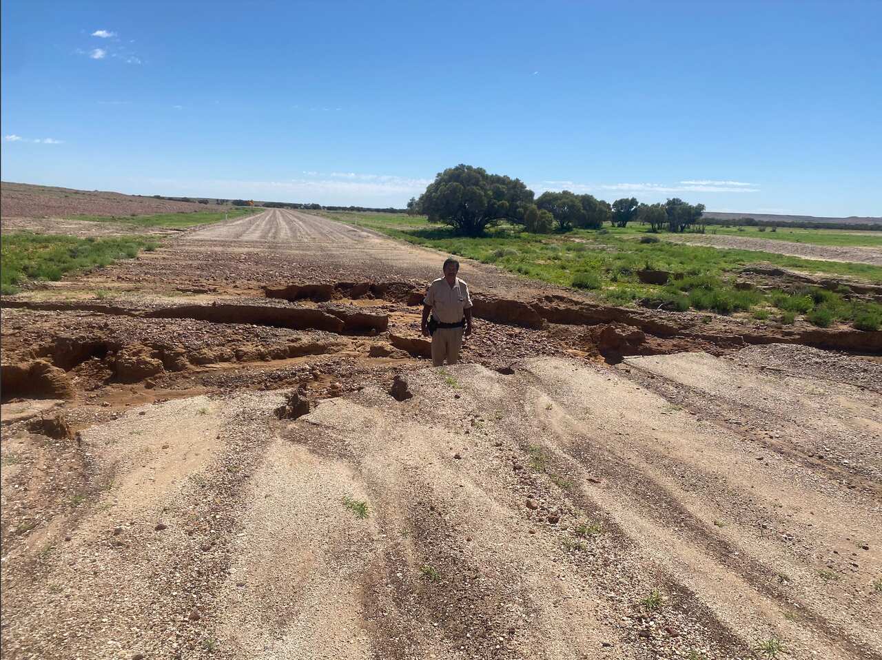A local Oodnadatta police officer stands on the damaged road in-between Coober Pedy and Oodnadatta, which remain cut-off.