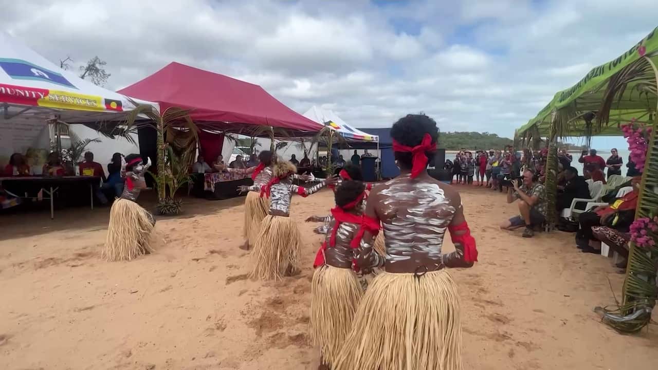 children dance in paint on the beach before assembled onlookers