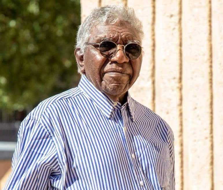An elderly aboriginal man in a blue and white striped shirt and chic sunglasses