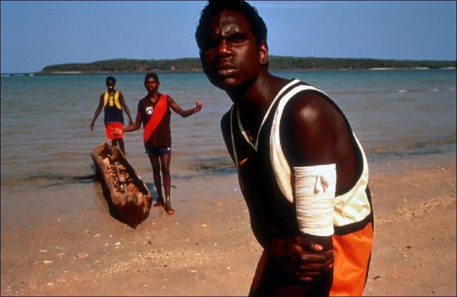 Three boys standing with their canoe in a bay.