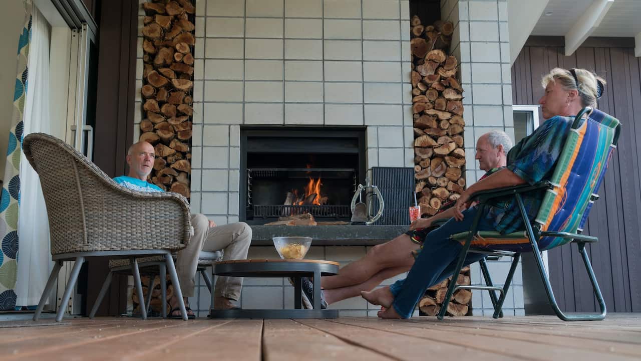 Three adults relax in outdoor fireplace setting at modern holiday home