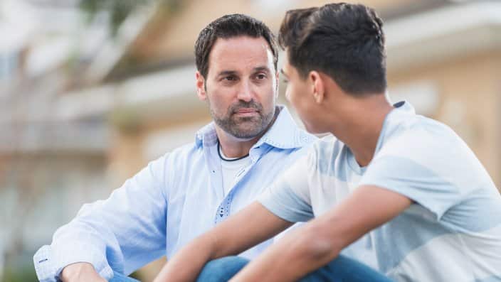 Father sitting with serious teenage boy