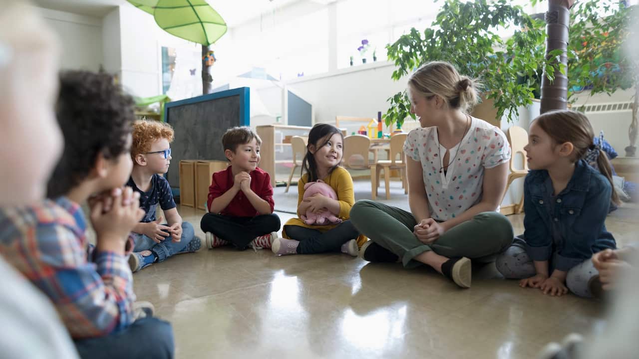Preschool teacher and students sitting in circle on floor in classroom