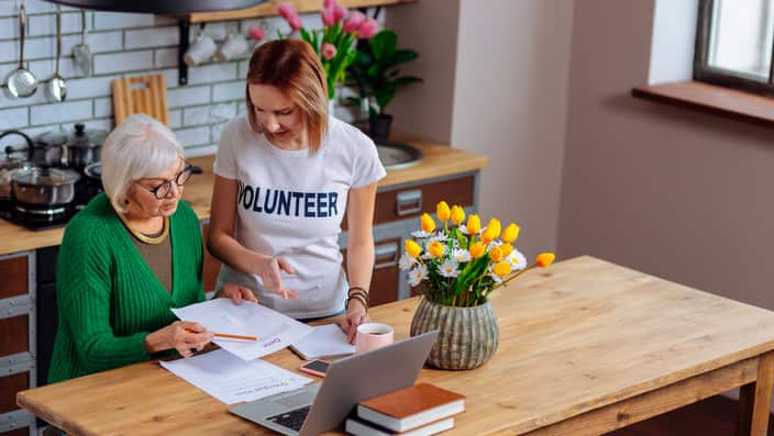 Lady volunteering in filling out paperwork for pensioner.