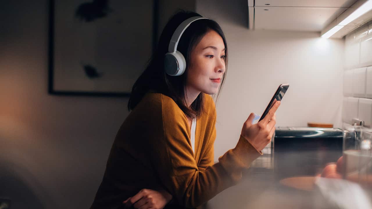 Woman With Bluetooth Headphones Listening To Music or podcasts On Smartphone
