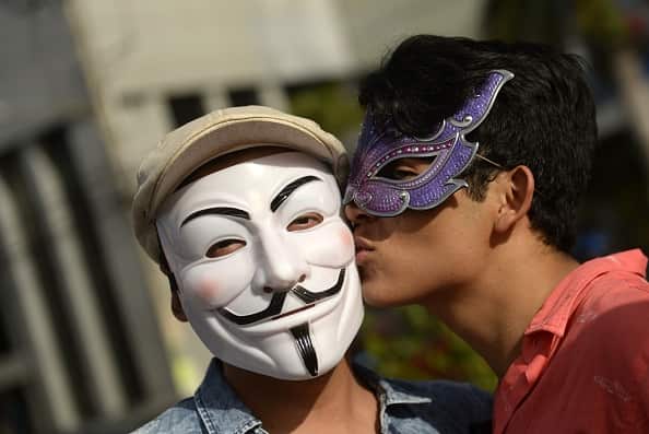 A reveler kisses another reveler wearing a Guy Fawkes mask during the Gay Pride Parade in San Salvador, El Salvador, on June 27, 2015. AFP PHOTO/ Marvin RECINOS        (Photo credit should read Marvin RECINOS/AFP/Getty Images)
