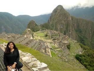 Young woman of Peruvian descent sitting with a view of Machu Picchu behind her.