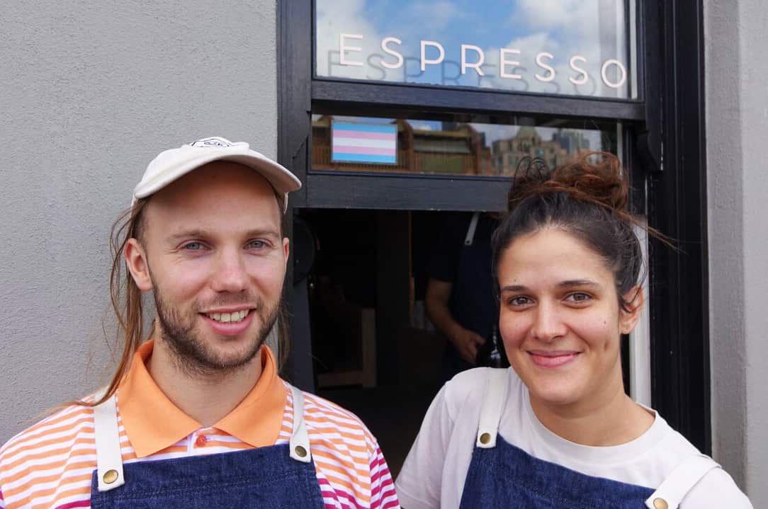 Chrissie and Zach stand in front of the transgender flag in the window of Assembly cafe.