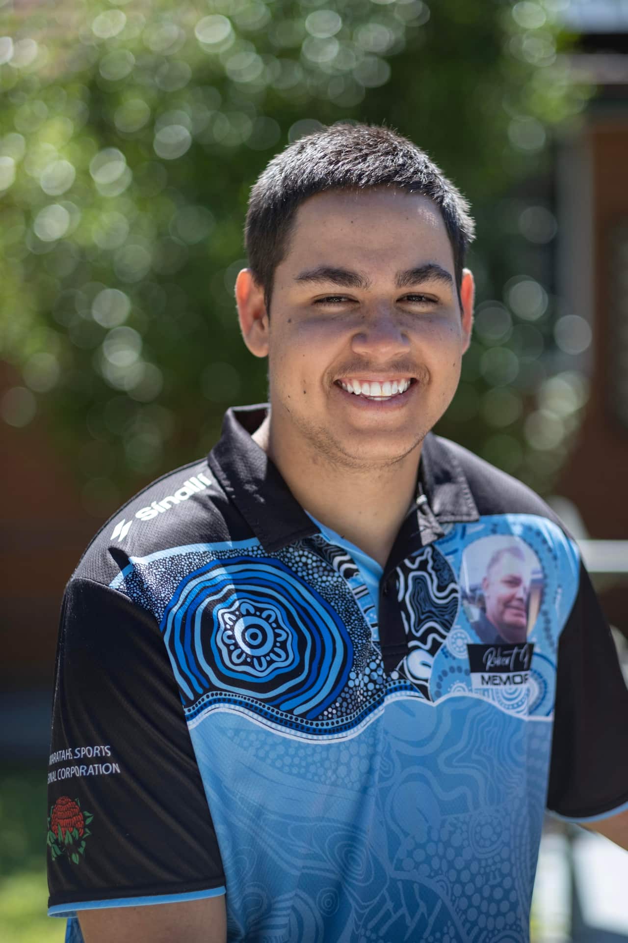 Image of a young man with a big smile standing outside in the sun