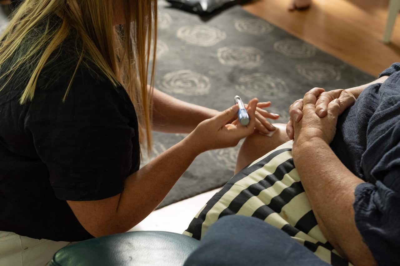 Image of a woman administering an injection on her mother's leg.
