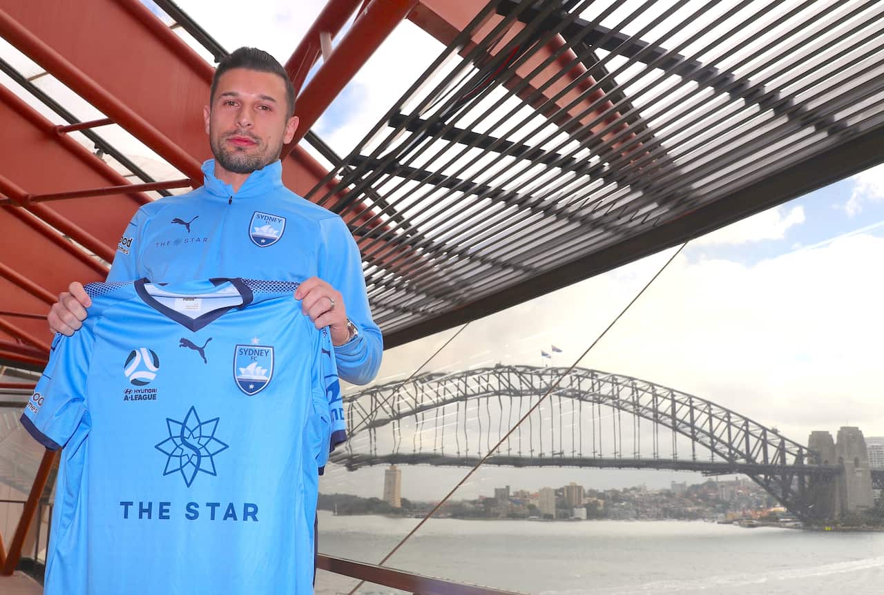 New Sydney FC player Kosta Barbarouses holds a team jersey after a media conference at the Sydney Opera House, Friday, June 7, 2019. (AAP Image/David Gray) NO ARCHIVING