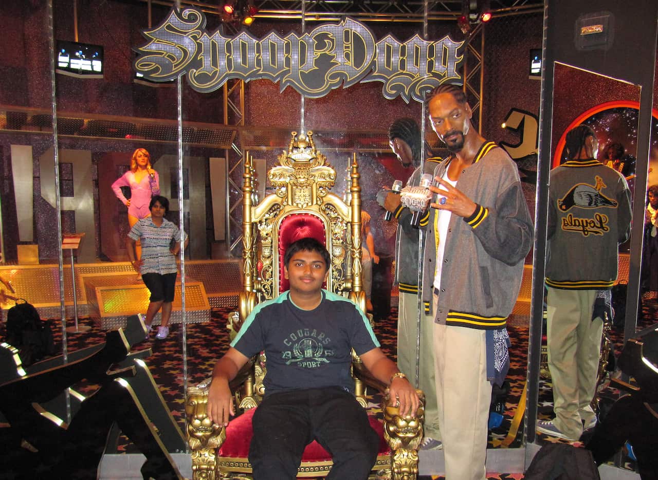 Boy sitting in a gold and velvet throne next to Snoop Dogg wax figure.