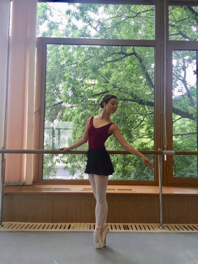 Emma Sullivan in a ballet studio wearing a red leotard, black skirt, pink tights and pointe shoes. 