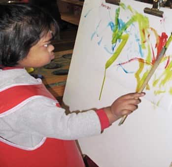 Young girl painting on a canvas with a paintbrush.