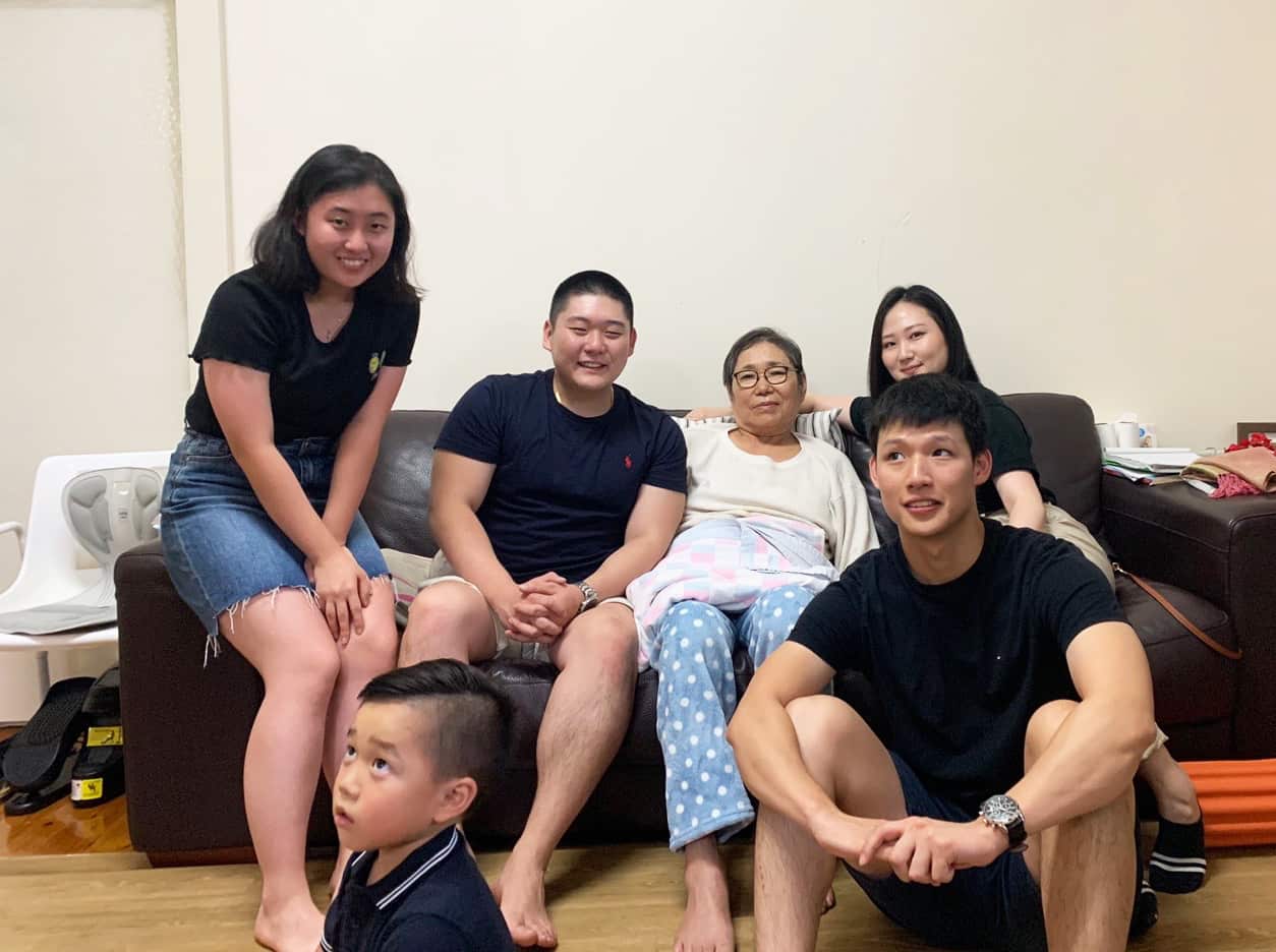 Three generations of Koreans sitting on the sofa and smiling at the camera.