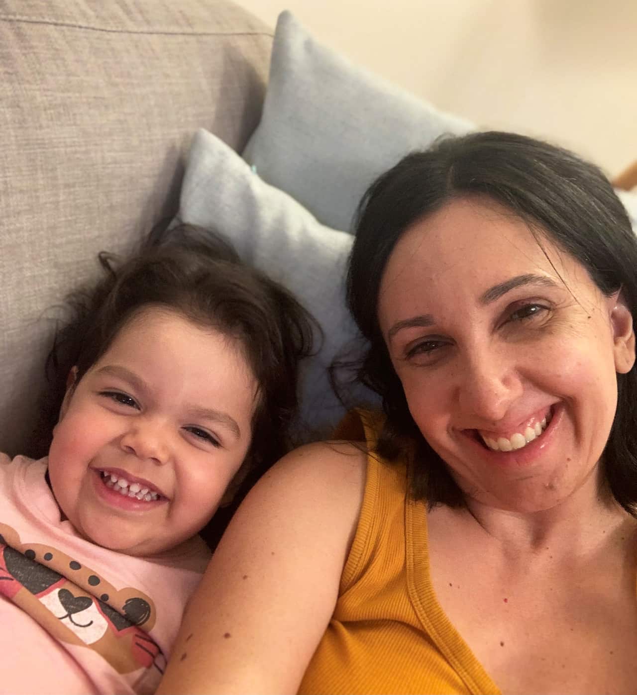 Toddler girl and mother on sofa, smiling at camera.