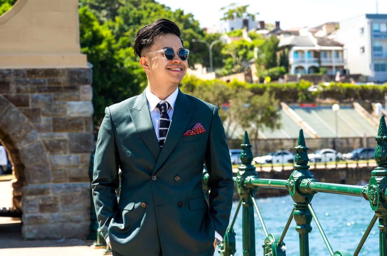 Young Asian man in sunglasses and green suit, smiling.