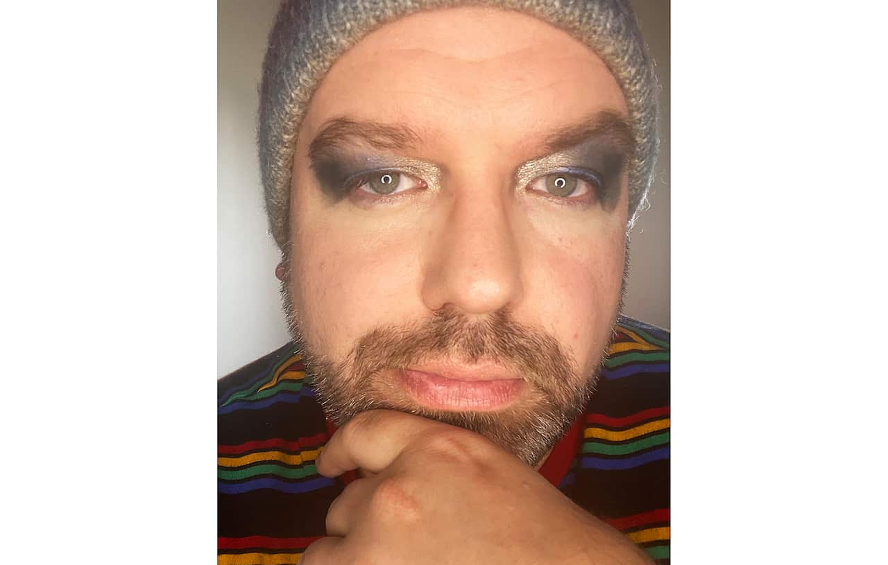 Gender diverse person wearing eyeshadow, beanie and rainbow striped shirt