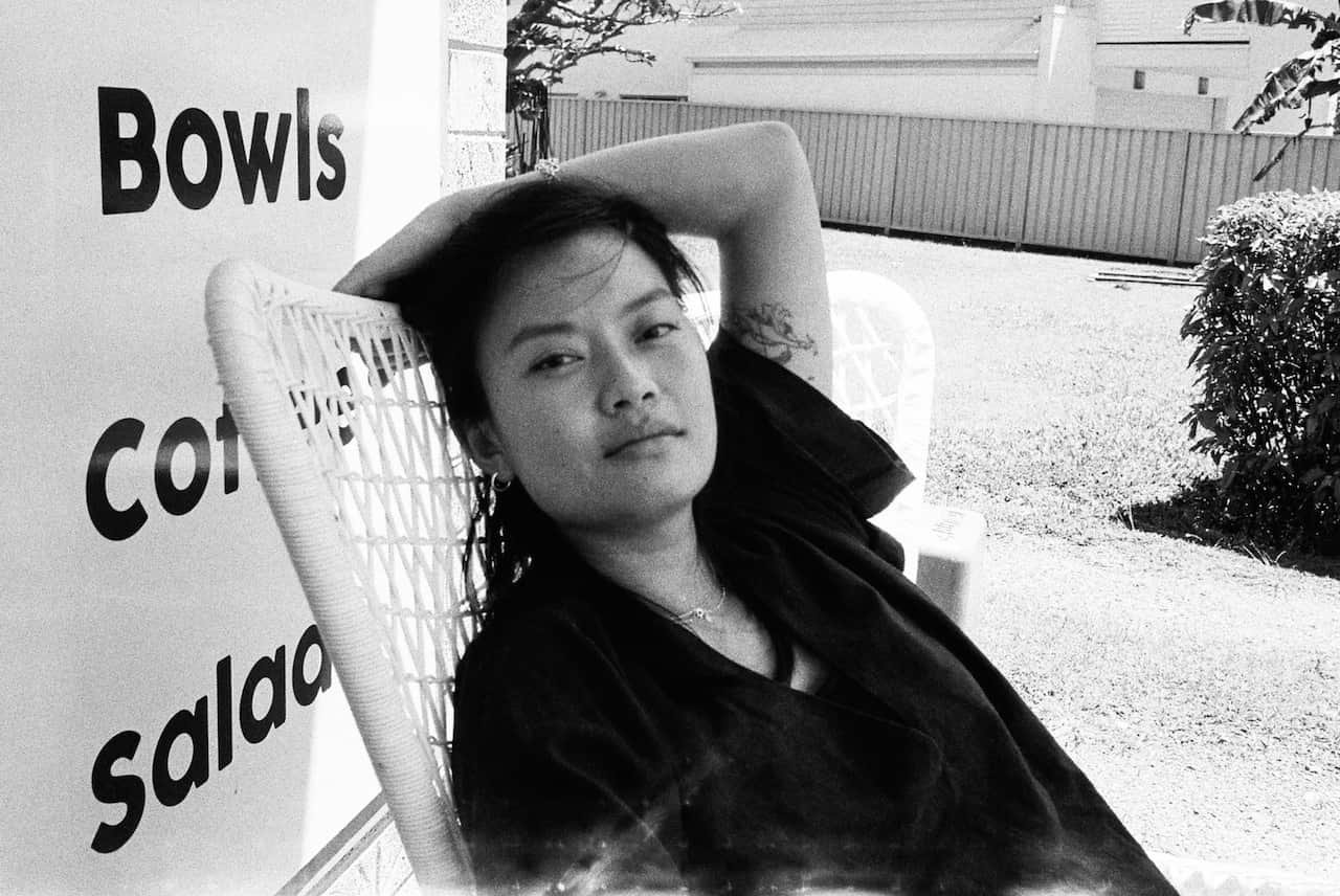 Black and white image of young Asian woman leaning back in chair looking at camera.