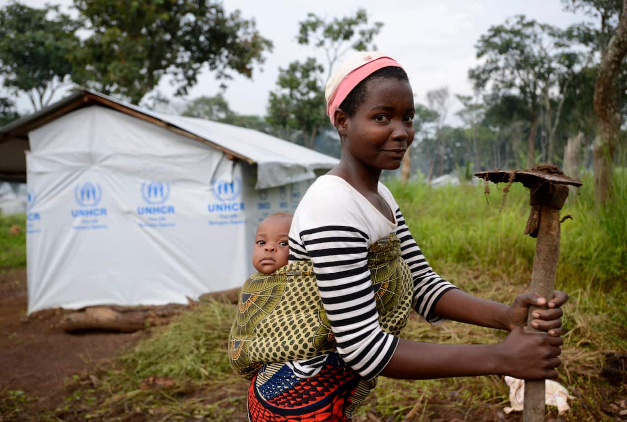 Burundi refugee mother carries her baby while she farms the plot of land that belongs to their shelter in the UNHCR refugee camp Nduta in the Kigoma district Tanzania. 