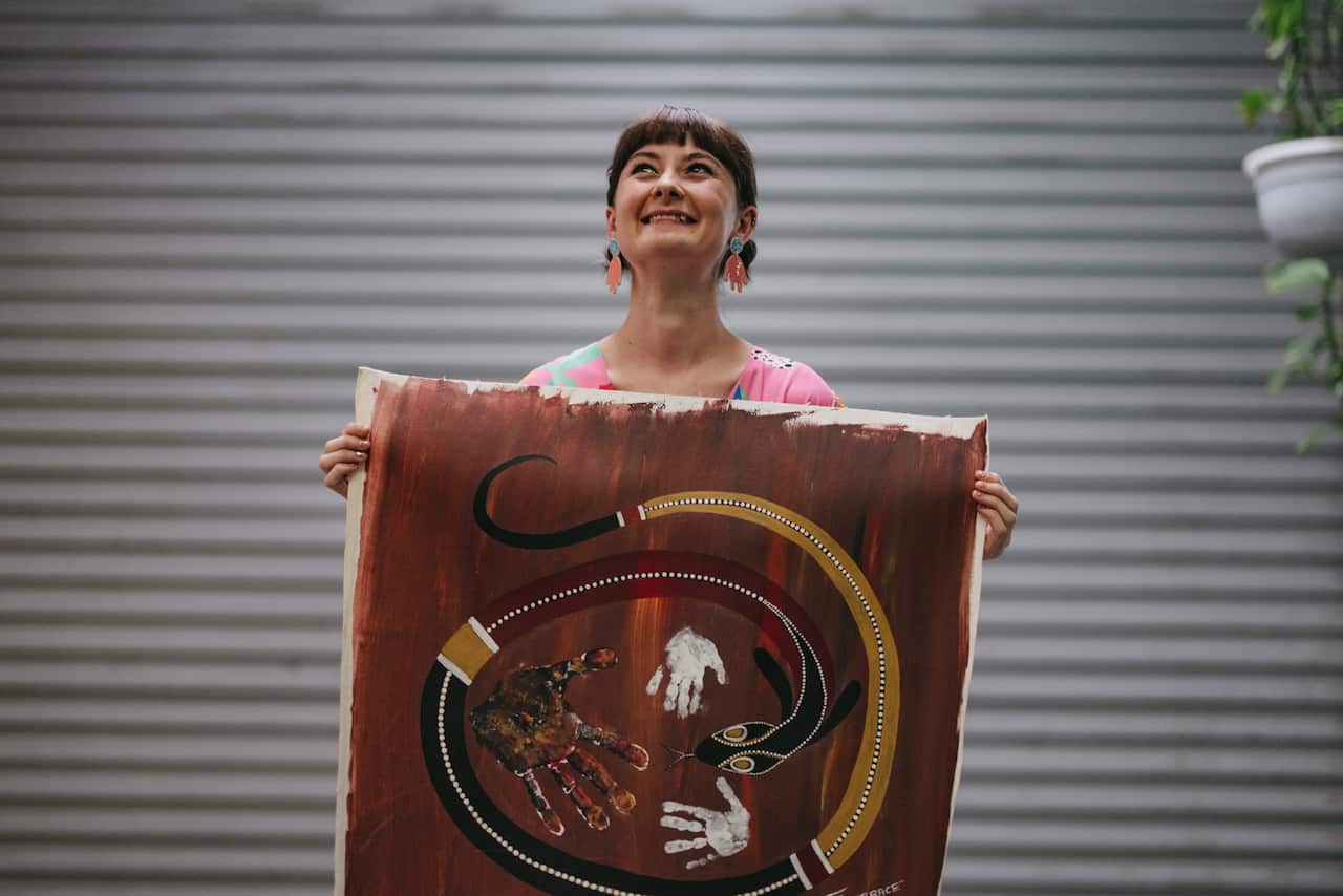 Nirrimi Firebrace holds up a painting she painted when she was young with her father and brother