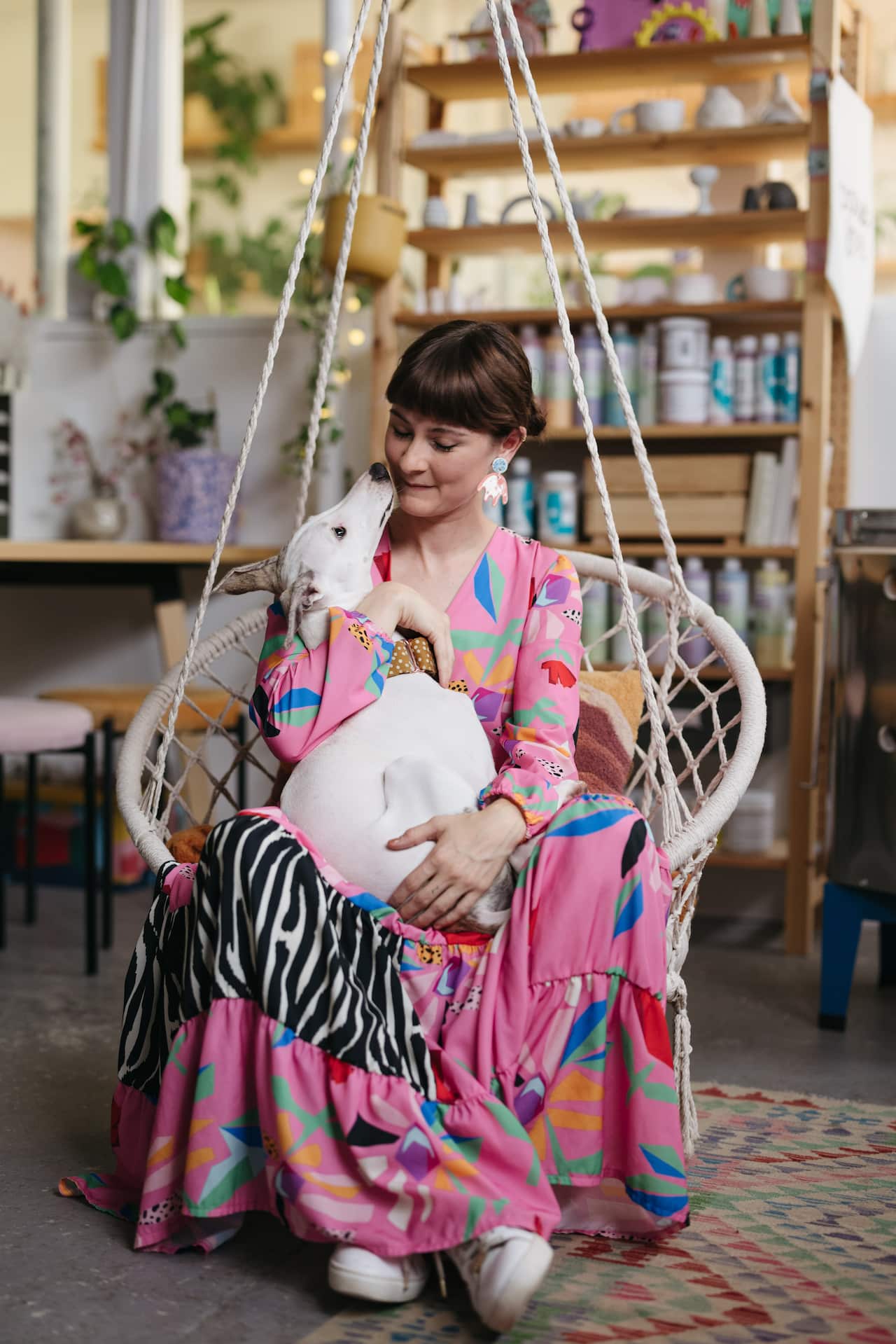 Nirrimi sits in a hanging chair with her dog Ru
