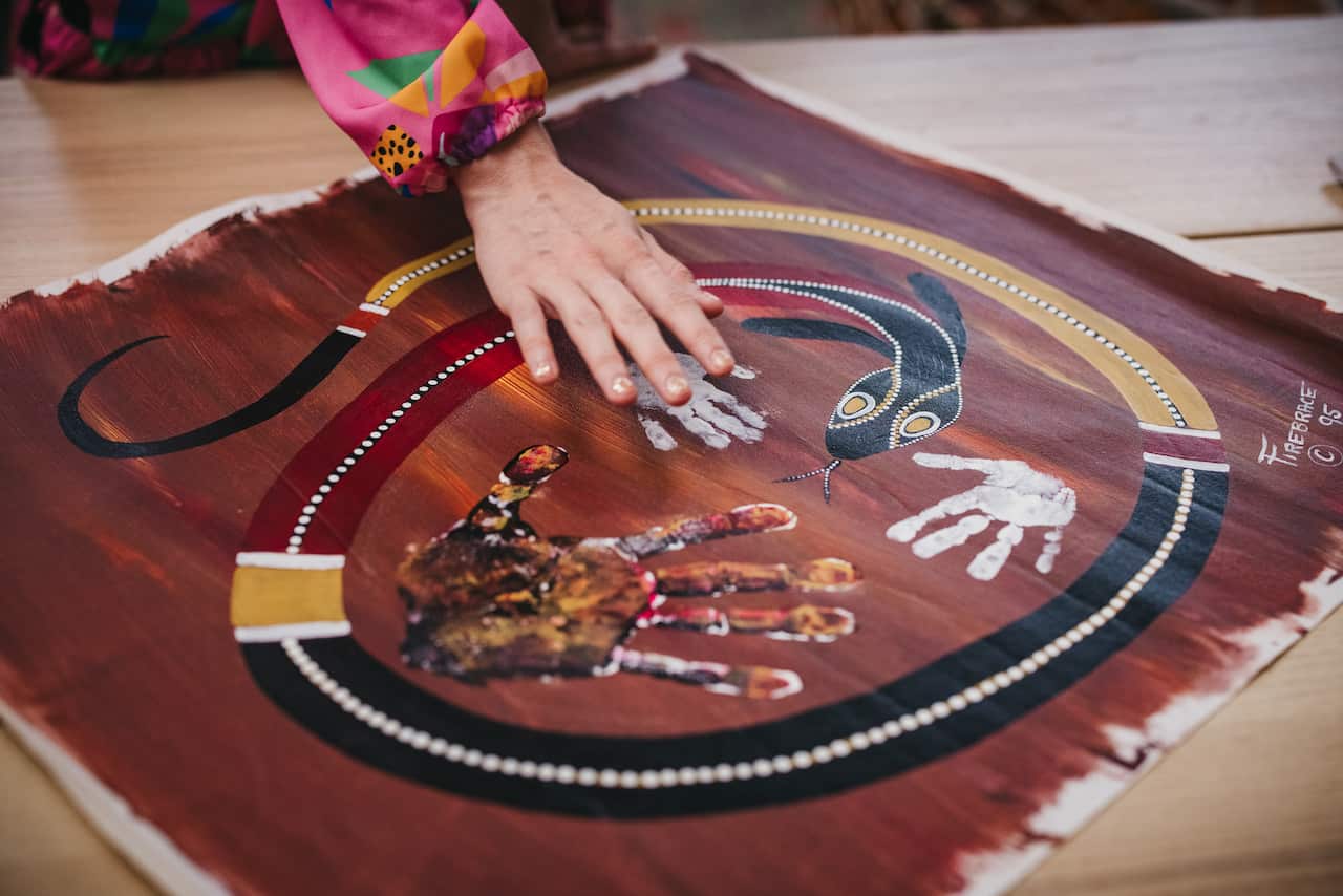 Nirrimi's hand hovers over her brother's small hand print on an Indigenous painting by her father