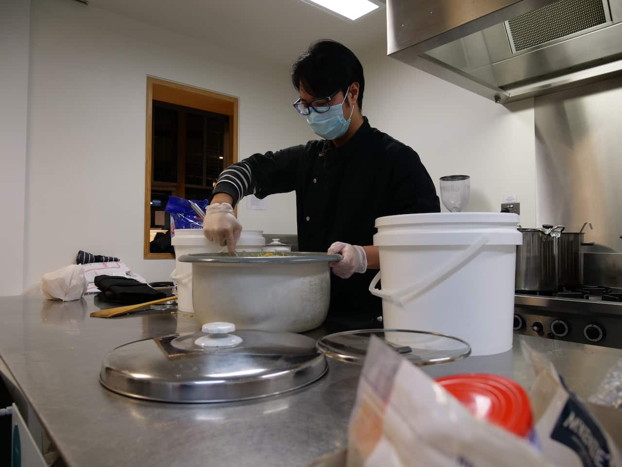 A young man wearing a mask stirring a big cooking pot
