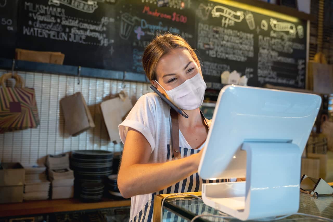 Waitress at a restaurant getting a delivery order on the phone and wearing a facemask