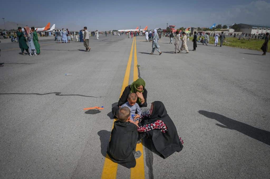 Afghan people sit as they wait to leave the Kabul airport in Kabul on 16 August, 2021. 