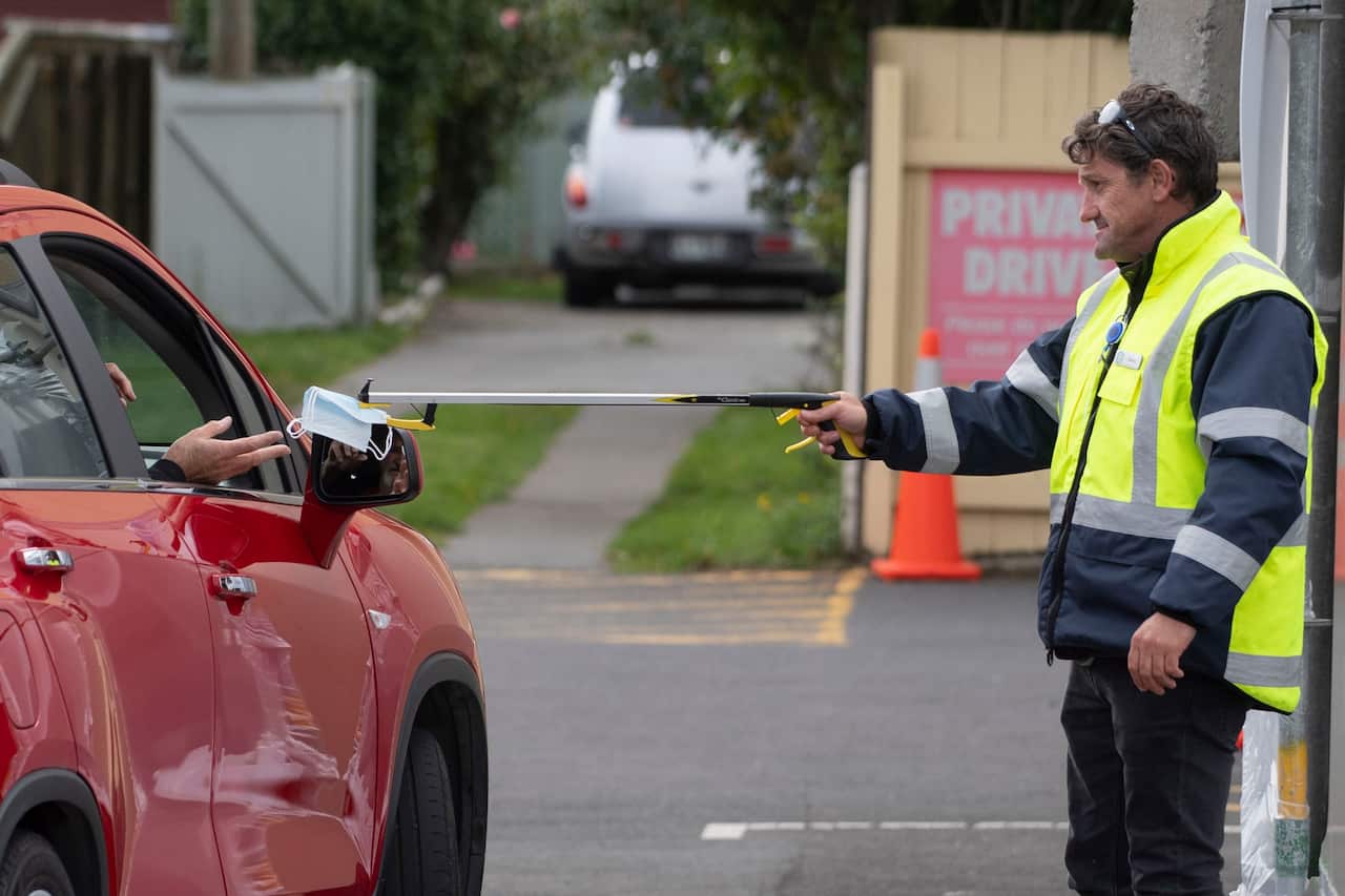 A security guard hands a face mask to a driver using a stick outside a COVID-19 clinic near Wellington.