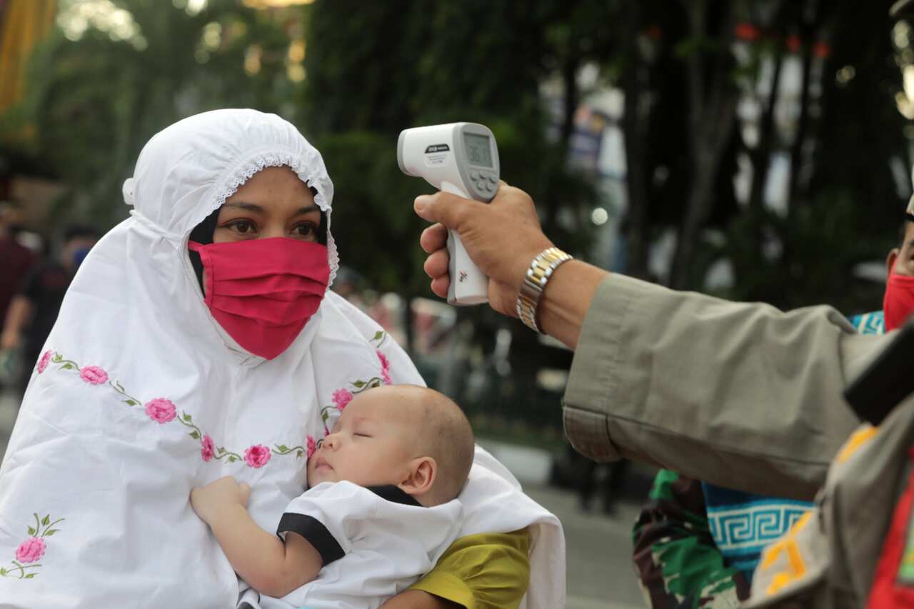 An Indonesian mosque official  checks the temperature of a worshipper before they enter Baiturrahman Grand Mosque for Eid al Fitr prayers in Banda Aceh, 